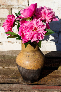乡土木桌上粘土壶里的粉红色牡丹花花束