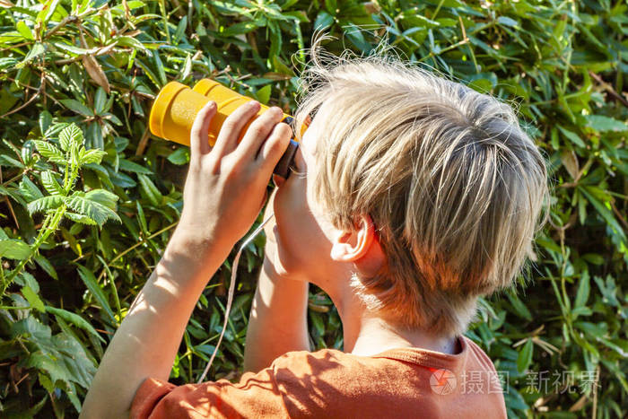 小男孩用望远镜看着绿色的篱笆