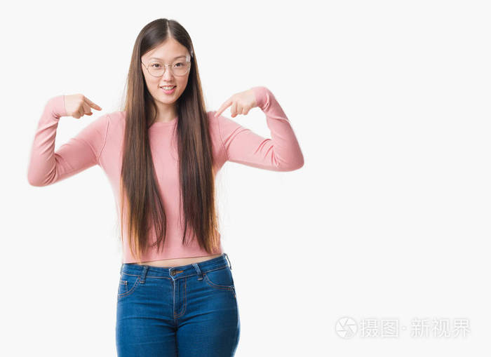 年轻的中国妇女在与世隔绝的背景下戴着眼镜, 脸上露出自信的笑容, 用手指自豪和快乐地指着自己。