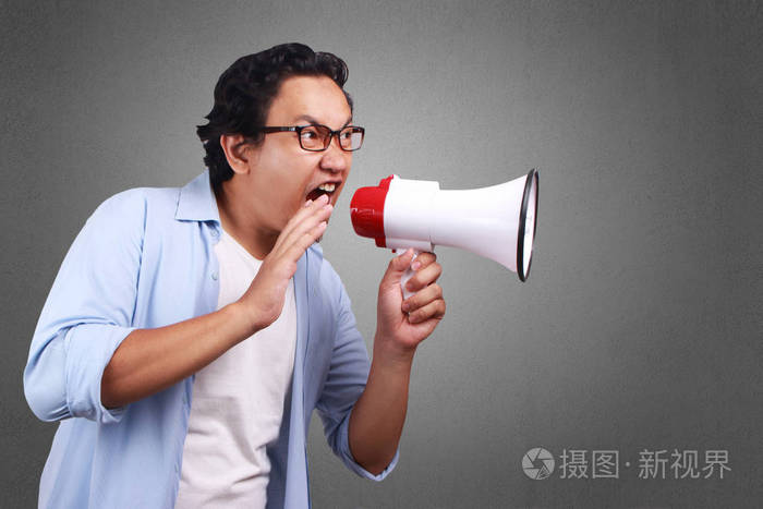 年轻的亚裔男子身穿白色和蓝色衬衫大喊用扩音器, 愤怒的表情.