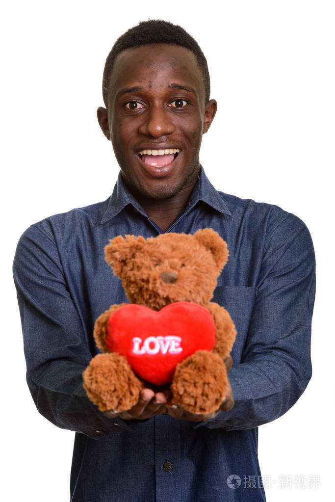 年轻快乐的非洲男人笑着给了泰迪熊的心