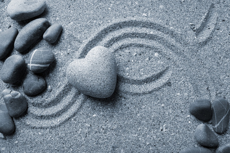 灰色的禅宗石在心，砂背景上的形状