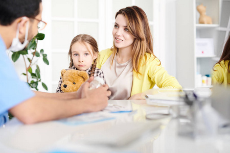 美丽的年轻母亲和可爱的小女孩的肖像访问医生, 并与儿科医生在咨询