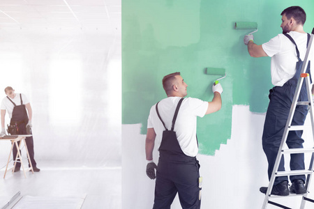 工人粉刷墙壁绿色和站在梯子上, 而完成室内
