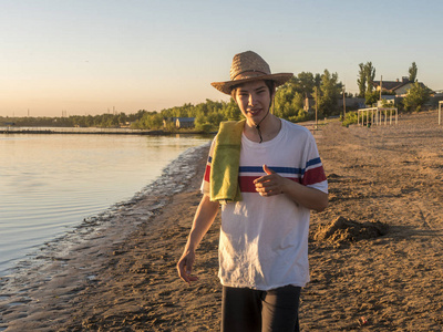 年轻微笑快乐少年在夏天帽子用毛巾在海海岸海滩在金黄小时