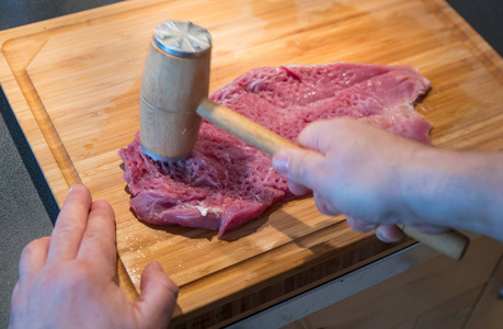 人准备美味的自制猪肉里脊肉与厨房锤在木制切割板上