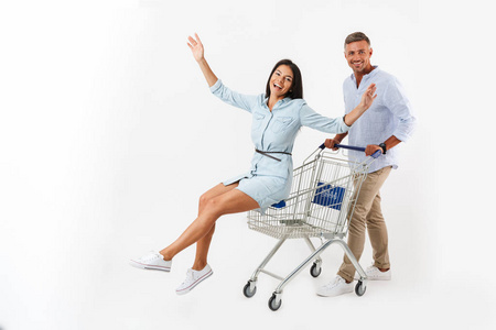 欢快的夫妇走在超市购物车, 快乐的女人坐在手推车远离孤立