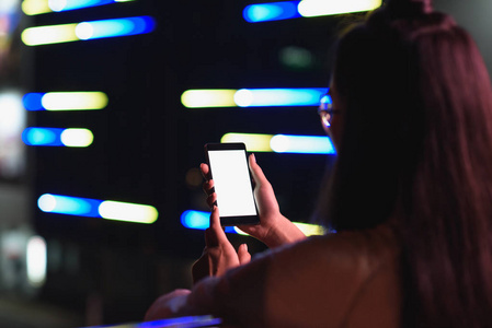 女孩拿着智能手机与白色空白屏幕在街上与霓虹灯在晚上的背景图, 未来概念的城市