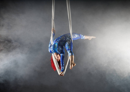 运动空中马戏团艺术家与红发在蓝色服装站在空中丝绸一只手