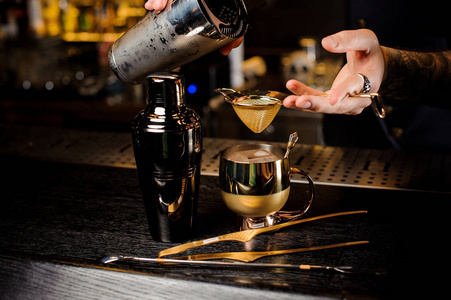 酒保倒新鲜可口的夏日饮料从振动筛到酒吧柜台上的老式铜杯