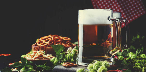 淡德国啤酒倒入大玻璃, 新鲜的绿色啤酒花和碗咸小吃和坚果, 秋季啤酒节的概念, 黑暗的背景, 选择性聚焦