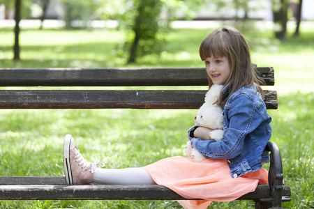 小女孩坐在公园的长椅上, 拿着她最喜欢的填充玩具