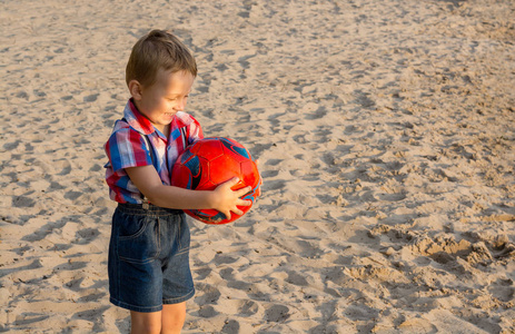 小男孩在海滩上用球, 他看着球和微笑