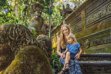 母亲和儿子坐在楼梯上与雕塑在巴厘岛的巴厘森林, 印度尼西亚