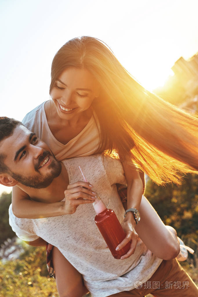 快乐的年轻夫妇享受无忧无虑的时间而男人背着漂亮的女人肩上