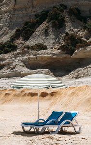 在马耳他一个偏僻的海滩上, 两把带绿色条纹的沙滩伞的蓝色甲板椅