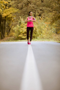 秋天在森林小径上奔跑的年轻健身妇女