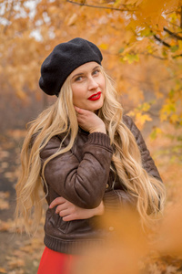 女孩金色的黑色贝雷帽与明亮的红唇对秋季花园的背景