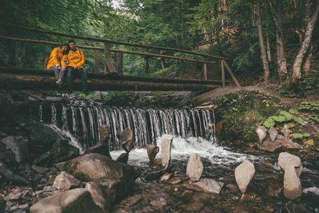 夫妇坐在木桥过河在森林。平衡的石头在底部。复制空间
