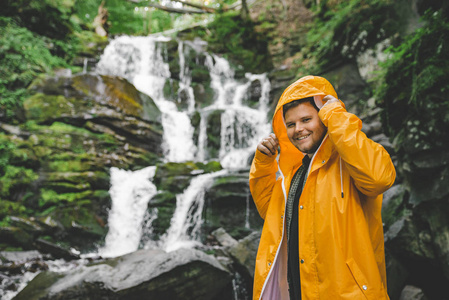 男子站在黄色的雨衣, 看着瀑布。徒步旅行概念