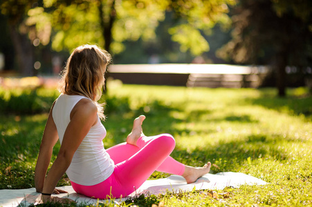 在阳光明媚的夏日公园草地上做瑜伽练习的年轻女子