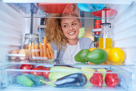 一个女人站在冰箱前, 装满了杂货, 看着吃的东西。从冰箱内部拍摄的照片