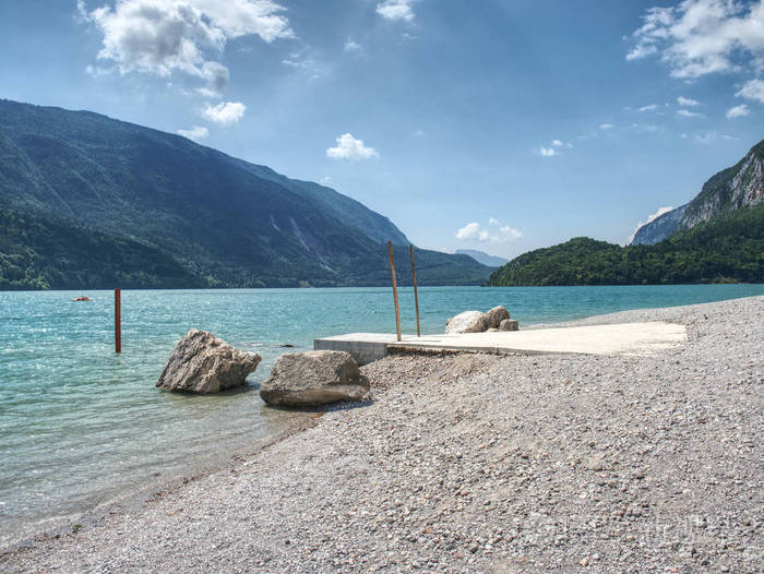 山湖的蓝绿色的水岸边的石头堆积.蓝色山在水位镜子