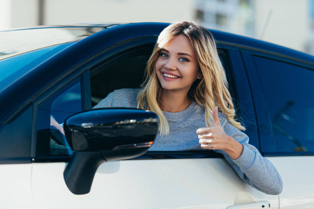 金发碧眼的微笑的女人的肖像显示拇指, 而驾驶汽车