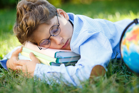 可爱的男孩穿着蓝衬衫的圆形眼镜睡在他的书在草地上的公园。教育, 回到学校概念