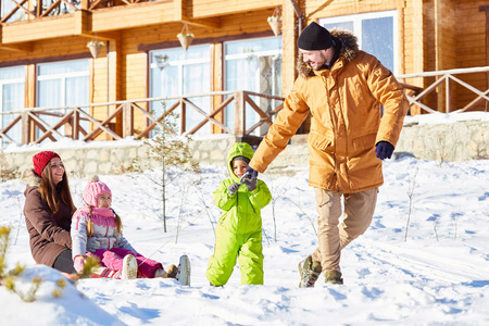 年轻的白种夫妇带着小孩子在阳光明媚的冬日里在娱乐区散步和拉雪橇