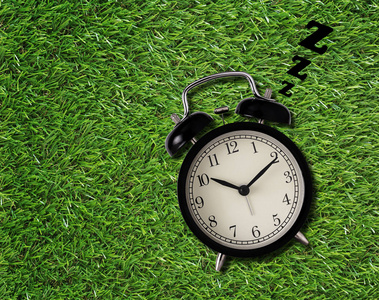 起床晚概念, 闹钟睡在绿草背景上