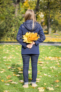 年轻的女孩在秋天的公园里拿着一个黄色的秋天的叶子在她的手后面她的后面
