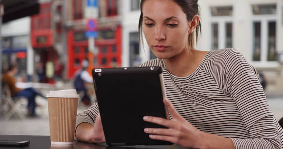千禧年妇女坐在咖啡馆桌上, 在城市咖啡馆外坐着平板电脑