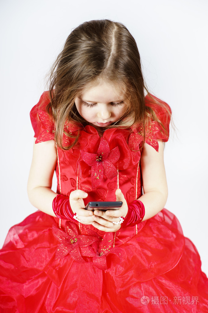 可爱的小女孩穿着玩智能手机的舞会礼服