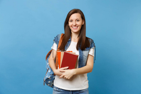 年轻快乐美丽的女学生画像牛仔服装与背包藏品学校书籍, 准备学习孤立的蓝色背景。中学大学的教育理念