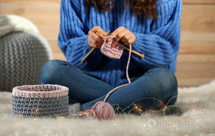 妇女在温暖的毛衣编织在蓬松的地毯在家里