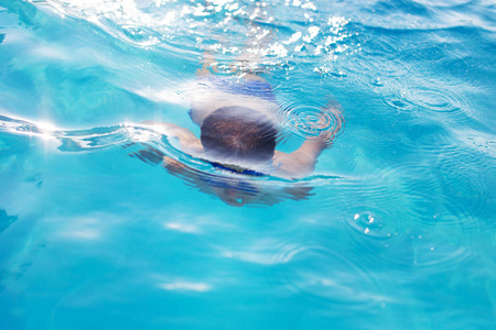 小男孩在水下游泳在游泳池室外照片