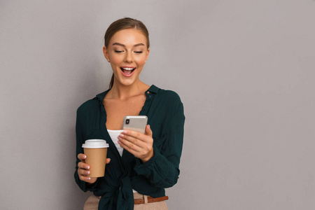 形象的兴奋美丽的商业妇女冒充查出的灰色墙壁背景饮用咖啡使用手机