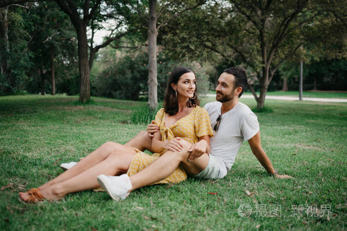 时尚可爱的黑发女孩坐在她的男朋友之间的腿之间的胡子接近对方在草地