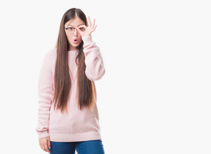年轻的中国妇女在独立背景戴眼镜做 ok 手势震惊与惊讶的脸, 眼睛看通过手指。不信的表达