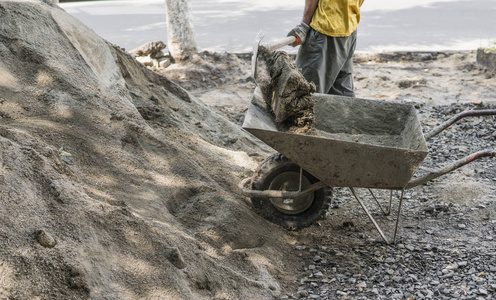 工人用铲子把手推车装满沙子, 用来建造人行道.建筑工具.
