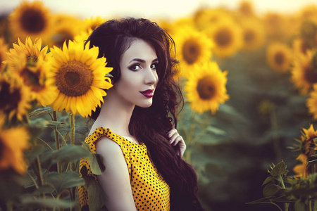 美丽的黑发妇女在黄色礼服在向日葵领域在日落
