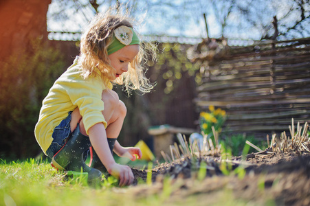 在阳光明媚的早期春天的花园里种花的黄色羊毛衫的可爱的孩子女孩