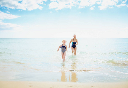 全长肖像微笑的现代母亲和儿童泳装跑出海边的海岸
