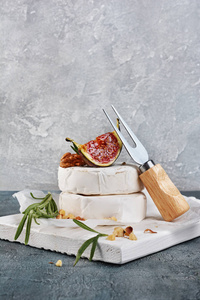 白色乳酪乳酪或乳酪与新鲜无花果, 坚果和迷迭香香料在木切削板和灰色具体背景的美食家开胃菜