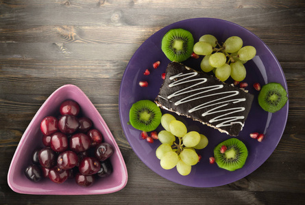 蛋糕和水果的甜点 葡萄, 猕猴桃, 石榴 在木背景。餐盘上的甜点