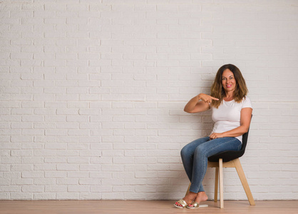 拉美裔妇女坐在椅子上的白色砖 walll 与惊讶的脸指向自己的手指照片