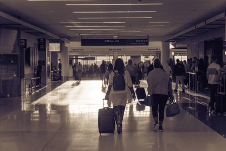 老式色调模糊繁忙的人群在机场步行与行李在清晨的光线。背景乘客或游客带行李离开走廊码头, 后视图