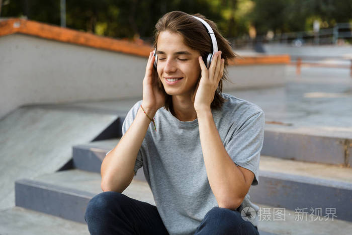 亲密的快乐的十几岁小男孩在滑板公园度过时光, 用耳机听音乐