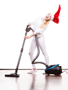 女人用真空吸尘器清理房子。有趣的年轻女孩，在圣诞老人的助手帽子与真空吸尘器。圣诞时间和家务劳动的概念